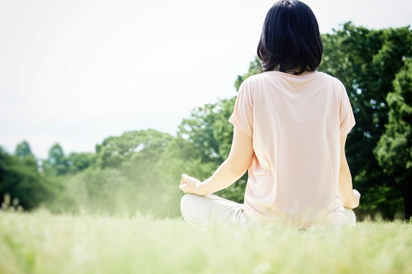 自然あふれる芝生の上で瞑想をする女性の後ろ姿